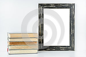 Empty black frame and stack of old books on white background