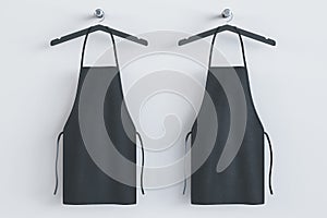 Empty black kitchen aprons on hangers. Light background. Chef and cooking concept. 3D Rendering
