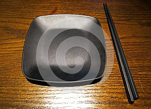 Empty black plate with chopsticks on the table