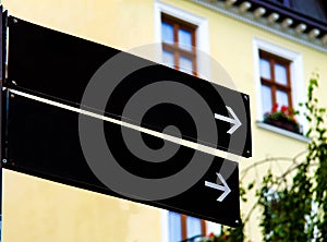 Empty black road signs or blank road signs showing direction against a building.