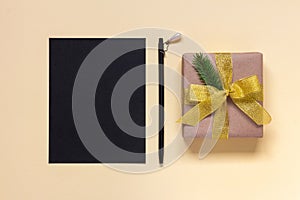 Empty black sheet of paper and pen near Christmas gift box with golden bow