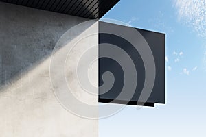 Empty black square stopper or banner hanging on concrete building with shadows and bright blue sky view. Bar, restaurant, shop and