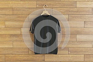 Empty black t-shirt hanging on wooden wall background. Ad, textile and fashion concept.