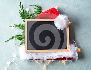 Empty blackboard background with santa cap and fir tree branches on gray with christmas star lights