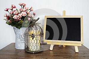 Empty blackboard with bird cage and flower in metal vase on wooden shelves