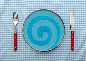 Empty blue ceramic plate with knife and fork