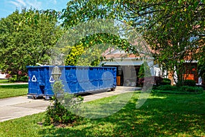 An empty blue dumpster in the driveway of a house with its garage door open in a residential community