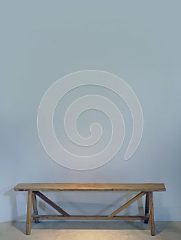 An empty blue grey color wall with a wooden bench against the wall, spotted lighting from above, empty space for copy or text