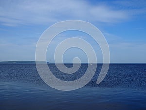 Empty Blue Ocean and Blue Sky in the distance a white sailboat and mountains covered with forest