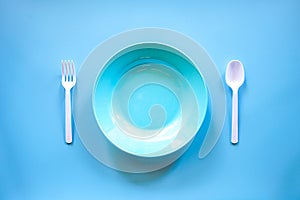 Empty blue plasstic dish with white plastic spoon and fork on blue background