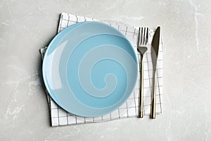 Empty blue plate with cutlery and napkin on grey marble table, flat lay