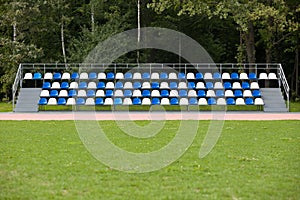 Empty blue and white seats in a footbal or soccer stadium. Grass field and plastic chairs, open door sports arena