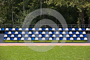 Empty blue and white seats in a football or soccer stadium. Grass field and plastic chairs, open door sports arena