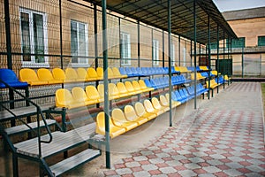 Empty blue and yellow sports seats of the grand stand at the back yard of school on the stadium