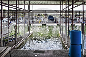 Empty boat slip in luxury boat dock at lake with other speedboats moored in distance - some up on racks and roller floater pad in