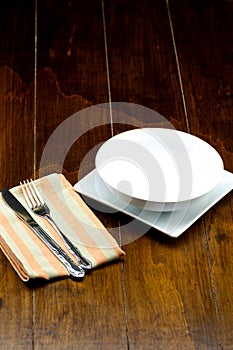 Empty bowl on square dish with fork and knife on napery.