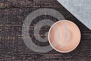 An empty bowl of white clay and a gray cloth napkin on an old wooden table surface
