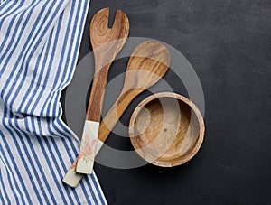 Empty bowl and wooden spoons on a black table, top view