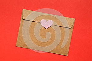 Empty brown craft envelope, sticker heart on red background. top view, copy space. Greeting card mockup Valentines Day