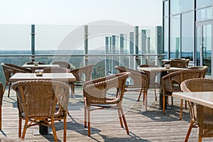 Empty cafe with rattan wicker armchairs and tables on summer garden terrace outdoor, free space. Table and chairs in empty cafe.