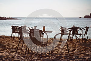 Empty cafe table and chairs on sandy beach in front of sea golf with clear sky before sunset