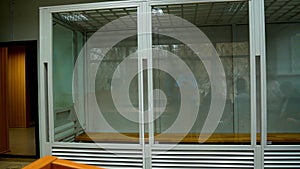 A cage with bulletproof glass for a suspect imprisoned in a courtroom. Panorama.