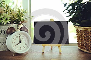 Empty card space for text message with wooden easel and alarm clock on wooden background