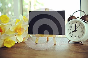 Empty card space for text message with wooden easel and alarm clock on wooden background