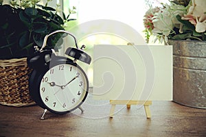 Empty card space for text message with wooden easel and alarm clock on wooden background