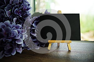 Empty card space for text message with wooden easel and flower bouquet on wooden background