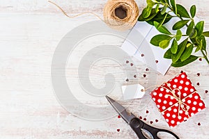 Empty card tied on red dotted gift box over white wood background. Copy space. Scattered heart shaped sequins, an envelope and wra