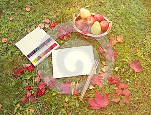 Empty card for your text, basket with fruits, watercolor paints, brushes for painting, autumn maple leaves and viburnum berriess