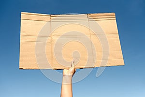 Empty cardboard held by one hand against a clear blue sky