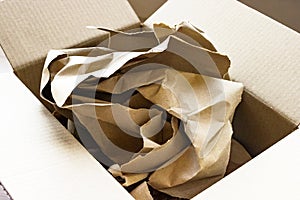 Empty cardboard shipping brown paper box with lid open with kraft packaging paper inside