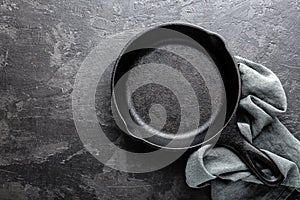 Empty cast iron frying pan on dark grey culinary background, view from above