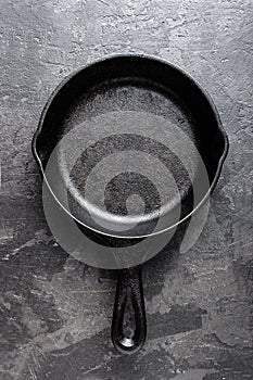 Empty cast iron frying pan on dark grey culinary background, view from above