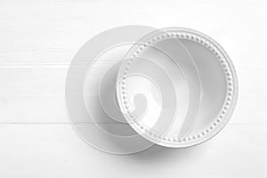 Empty ceramic bowl on white wooden table, top view. Space for text