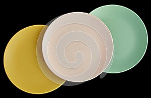 Empty ceramic plates of different colors laid out in a diagnal line on a black background