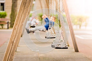 Empty chain swings in a playground. Blured background of swinging kids.