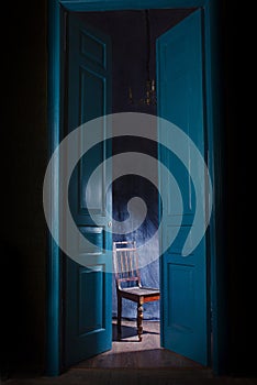 Empty chair in light behind blue massive vintage doors indoor.
