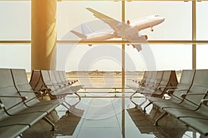 Empty chairs in the departure hall at airport on background of airplane taking off at sunset. Travel concept