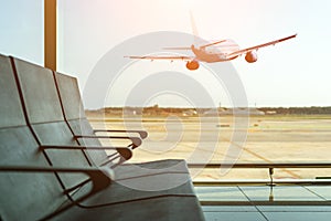 Empty chairs in the departure hall at airport on background of airplane taking off at sunset. Travel concept