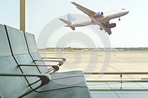 Empty chairs in the departure hall at airport on background of airplane taking off. Travel concept