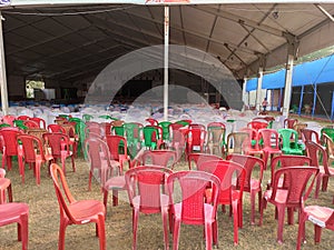 Empty chairs of red green and brown color lying in the tent disorganised.