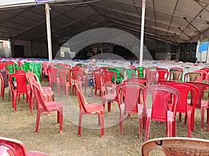 Empty chairs of red green and brown color lying in the tent disorganised.