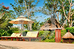 Empty chaise lounges with yellow-white striped mattresses that stand under a sun umbrella with the same pattern. Sanya, Hainan.