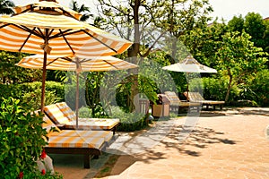 Empty chaise lounges with yellow-white striped mattresses that stand under a sun umbrella with the same pattern. Sanya, Hainan.