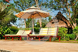 Empty chaise lounges with yellow-white striped mattresses that stand under a sun umbrella with the same pattern. Sanya, Hainan.