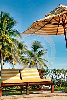 Empty chaise lounges with yellow-white striped mattresses that stand under a sun umbrella with the same pattern. Sanya, Hainan.