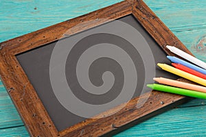 empty chalkboard with copyspace and colorful crayons on wooden table